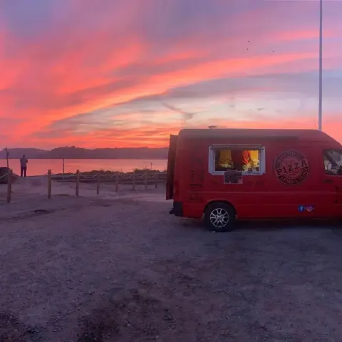 Ferdie the pizza van parked on the beach under a pink sunset