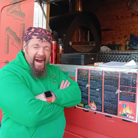 Simon laughing beside the wood fired oven in the back of the van