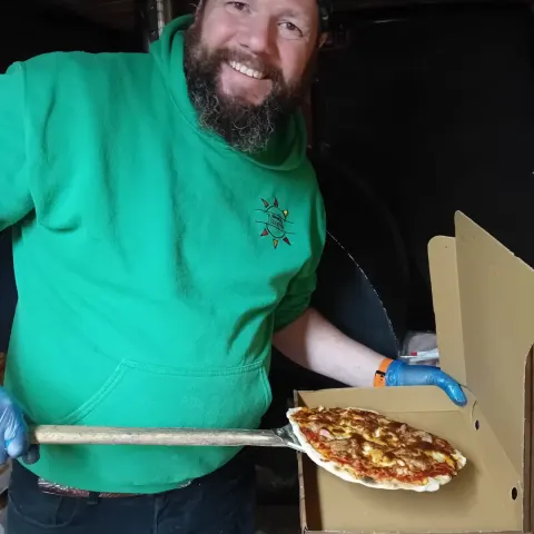 Simon sliding a pizza out of the oven on the peel