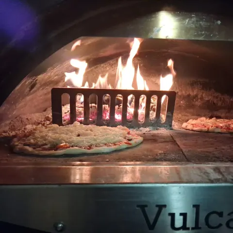 A pizza blistering in the Vulcan oven, flames curling over the dome